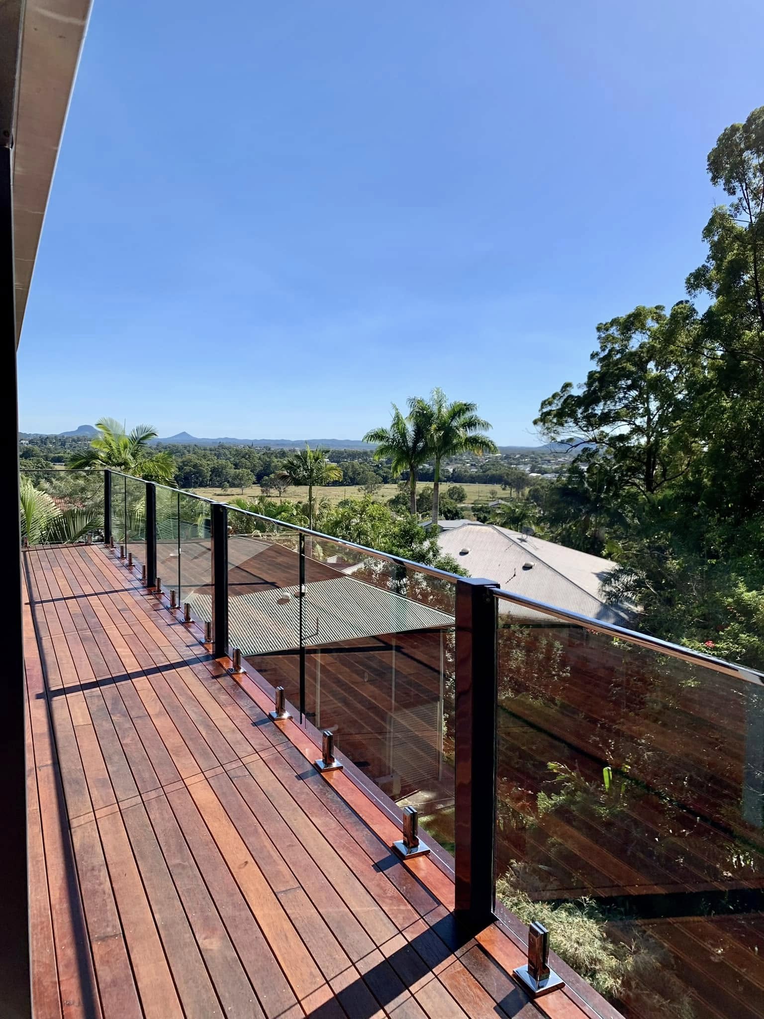 Frameless glass balustrade on an elevated second-storey timber deck with hinterland views